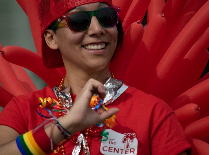 a person wearing sunglasses and decorated in pride gear smiling
